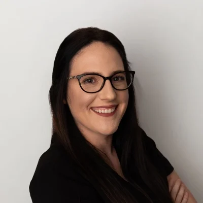 Staff Member Anna Smiling In Black Scrubs Against Grey Wall