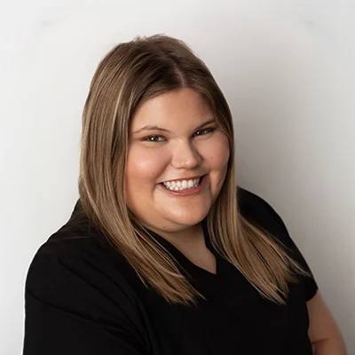 Staff Member Jaq Smiling In Black Scrubs Against Grey Wall