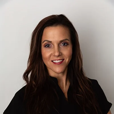 Staff Member Victoria Smiling In Black Scrubs Against Grey Wall